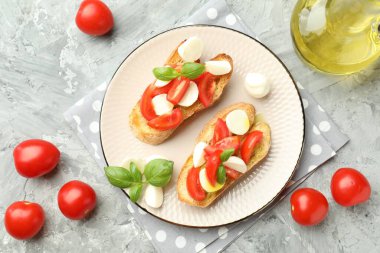 Mozarella peynirli lezzetli bruschettalar, domates ve fesleğen gri desenli masa, düz uzanmış