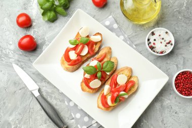 Mozarella peynirli, domatesli, fesleğenli ve baharatlı lezzetli bruschettalar gri desenli masa, düz yatak