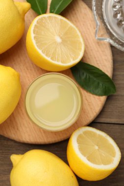 Bardakta limon suyu, yapraklar, meyve sıkacağı ve ahşap masada taze limon.