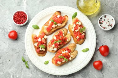 Mozarella peynirli, domatesli, fesleğenli ve baharatlı lezzetli bruschettalar gri desenli masa, düz yatak