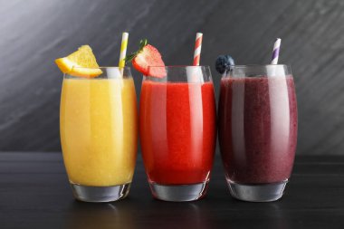 Siyah ahşap masadaki malzemelerle bardaktaki farklı lezzetli içecekler.