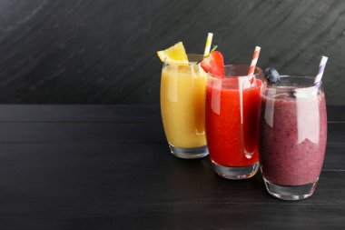 Siyah ahşap masadaki malzemelerle bardaktaki farklı lezzetli içecekler.