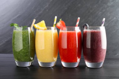 Siyah ahşap masadaki malzemelerle bardaktaki farklı lezzetli içecekler.