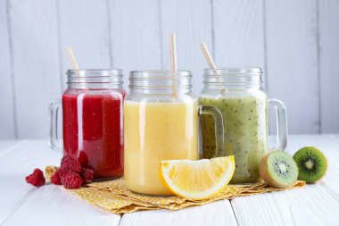 Mason kavanozlarında farklı lezzetli içecekler ve beyaz ahşap masada malzemeler.