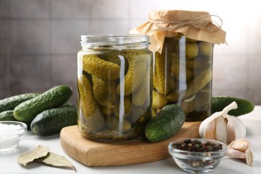 Kavanozda turşular, beyaz masada taze salatalık ve baharatlar, yakın plan.