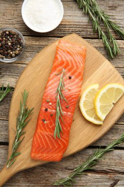 Bir parça somon fileto, baharatlar ve limon ahşap masada, düz uzanmış.