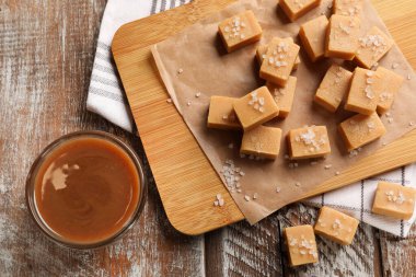 Tuzlu ve karamel soslu lezzetli şekerler ahşap masa üzerinde, düz yerde.