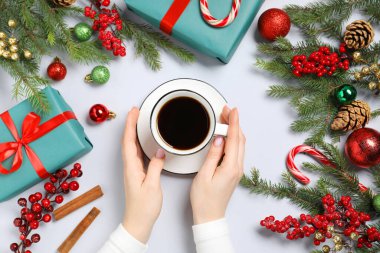 Bir fincan aromatik kahve, köknar ağacı dalları, hediye kutuları ve beyaz arka planda Noel dekoru olan bir kadın.