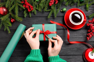 Hediye kutusu olan bir kadın, aromatik kahve ve siyah ahşap masada Noel dekoru.