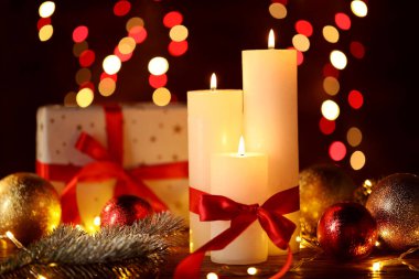 Yakıcı mumlar, köknar ağacı dalları, takılar ve ahşap masa üzerindeki şenlikli ışıklar, bulanık ışıklı siyah arka plan, yakın çekim. Bokeh etkisi