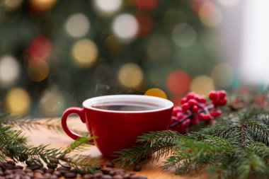 Kahve fincanı, fasulye ve köknar dalları ahşap masada bulanık ışıklara karşı, yakın çekim. Noel tebrik kartı.