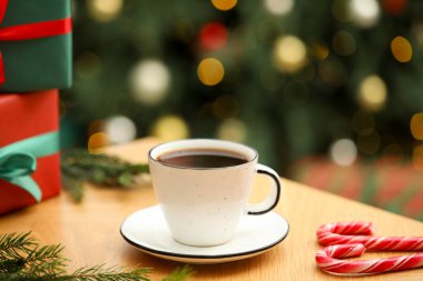 Fincanda romatik kahve, köknar ağacı dalları, şeker kamışları ve ahşap masada bulanık ışıklara karşı hediye kutuları, yakın çekim. Noel tebrik kartı.