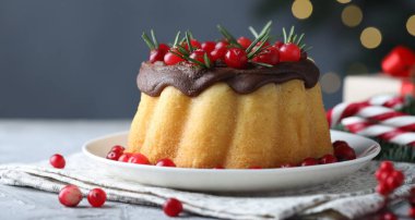 Çikolata kaplı lezzetli Noel pastası, gri desenli masada kızılcık ve biberiye, bulanık ışıklara karşı, yakın plan. Bokeh etkisi