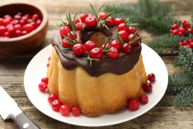 Çikolata kaplı lezzetli Noel pastası, kızılcık, biberiye ve köknar ağacı dalları ahşap masada, yakın plan.