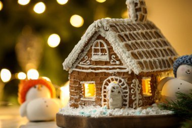 Üzerinde krema, şeker, pudra şekeri ve Noel süsü olan güzel zencefilli ev bulanık ışıklara karşı, yakın plan. Metin için boşluk