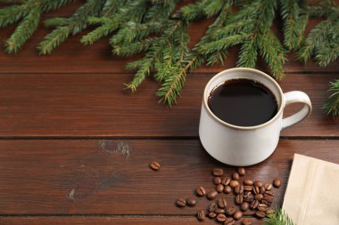 Aromatic coffee in cup, beans and fir tree branches on wooden table, closeup. Space for text
