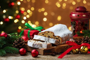 Geleneksel Noel Stollen şekerli, baharatlı ve ahşap masa üzerindeki şenlikli süslemeli bulanık ışıklara karşı, yakın çekim. Bokeh etkisi