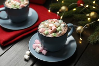 Lezzetli sıcak kakao içeceği bardakta marşmelov ve karanlık ahşap masada Noel dekoru, yakın plan.