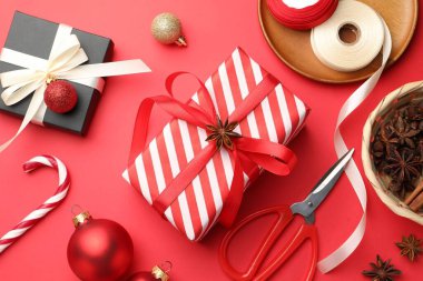 Kutlama ambalajı. Hediye kutuları, kurdele, makas, ambalaj kağıdı ve kırmızı arka planda Noel dekoru, düz yatış