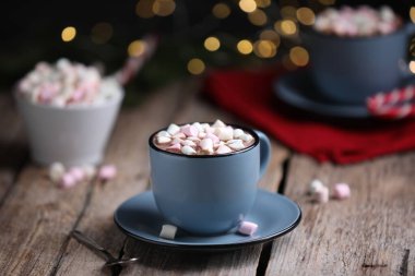 Ahşap masada lokum kaplı lezzetli kakao bulanık Noel ışıklarına karşı, yakın plan.