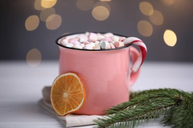 Lezzetli kakao, şekerleme kamışı, kurutulmuş portakal dilimi ve köknar dalı beyaz ahşap masa üzerinde bulanık Noel ışıklarına karşı, yakın çekim