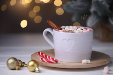 Marşmelovlu, tarçınlı, bastonlu ve beyaz ahşap masada bulanık ışıklara karşı Noel süslü lezzetli kakao, yakın plan. Metin için boşluk
