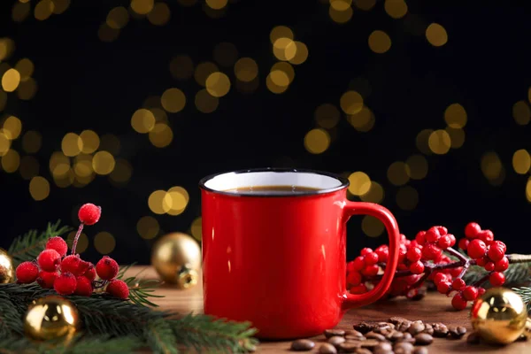 Kırmızı bardakta romatik kahve, fasulye, böğürtlen ve köknar ağacı dalları ahşap masada siyah arka planda bulanık ışıklarla, yakın plan. Noel tebrik kartı.