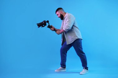 Açık mavi arkaplanda kameralı titreşim dengeleyici kullanan kameraman