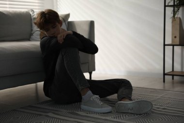 Evdeki kanepenin yanındaki depresyondaki genç çocuk.