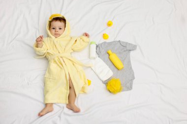 Bornozlu şirin bir bebek, banyodaki aksesuarlar ve giysiler, üst manzara.