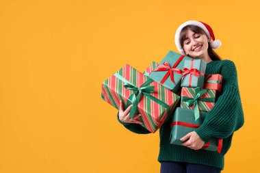 Sarı arka planda bir sürü hediye kutusu olan, Noel Baba şapkalı gülümseyen kadın, mesaj için yer. Noel ve Yeni Yıl Kutlaması