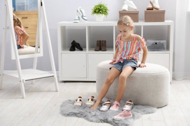 Küçük kız dükkanda farklı ayakkabılar deniyor.