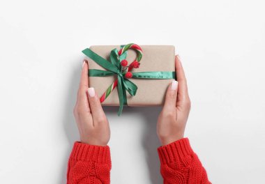 Elinde süslü Noel hediyesi olan beyaz arka planda baston şekerli bir kadın.