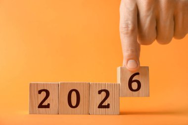 Yeni 2026 yılı. 6 numaralı küpü turuncu arka plana koyan adam, yakın plan.