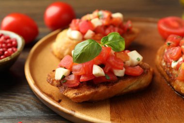 Domatesli lezzetli bruschettalar, mozzarella peyniri ve fesleğen ahşap masada servis edilir, yakın plan.