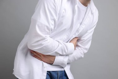 Gri arka planda mide ağrısı ve bulantı çeken adam, yakın plan.