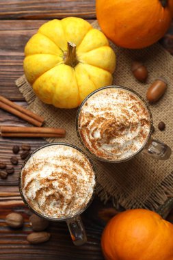 Cam bardaklarda krem şantili, ahşap masada malzemeli lezzetli balkabaklı latte.