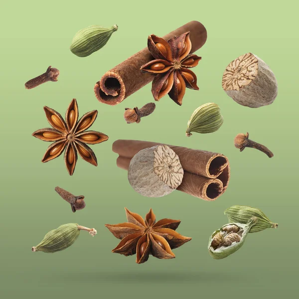 Noel içecekleri için farklı baharatlar ve yeşil arkaplana düşen yemekler. Anason, kakule, tarçın, hindistan cevizi ve karanfil.