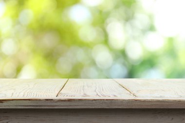 Dışarıdaki boş tahta masa. Arka planda bulanık yeşillik. Tasarım için boşluk