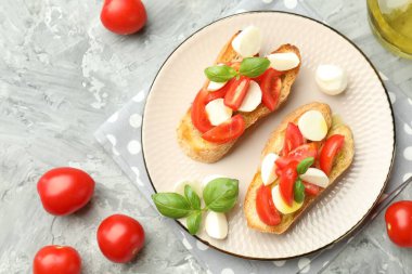 Mozarella peynirli lezzetli bruschettalar, domates ve fesleğen gri desenli masa, düz uzanmış