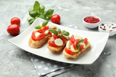 Mozarella peynirli, domatesli, fesleğenli ve baharatlı lezzetli bruschettalar. Gri desenli masa, yakın plan.