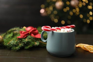 Lezzetli sıcak kakao, şekerleme kamışı, köknar ağacı dalı ve ahşap masada kurumuş portakal dilimleri bulanık Noel ışıklarına karşı, yakın çekim