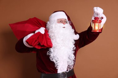 Kırmızı çantalı Noel Baba ve kahverengi arka planda fener.