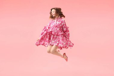 Pembe arka planda atlayan güzel giyimli genç bir kadın.