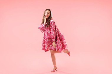 Pembe arka planda poz veren güzel giyimli genç bir kadın.