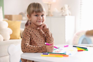 Beyaz masa içinde keçeli kalemle çizen sevimli küçük kız.
