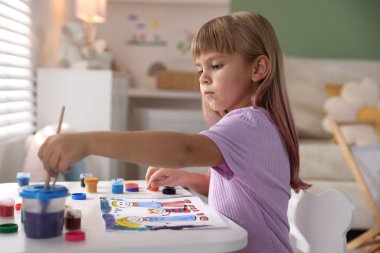 Beyaz masa içinde fırça çizen küçük kız.