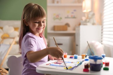 Beyaz masa içinde fırça çizen küçük kız.