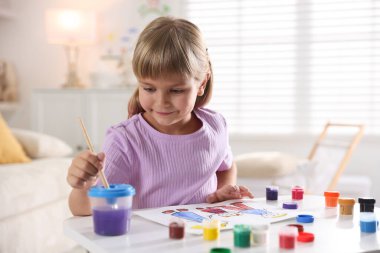 Beyaz masa içinde fırça çizen küçük kız.