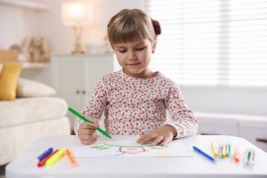 Beyaz masa içinde keçeli kalemle çizen sevimli küçük kız.